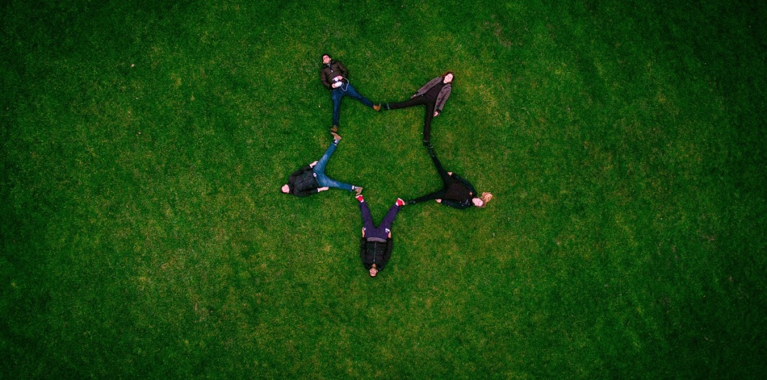 People sitting down on the grass forming a star together